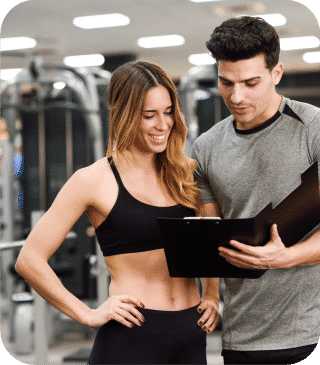 Em uma academia, uma mulher com roupas de treino sorri ao lado de um homem com uma prancheta