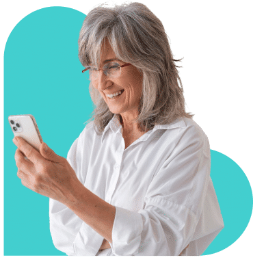 Mulher sorridente com cabelos grisalhos e óculos, segundo o seu smartphone. O fundo apresenta uma forma azul clara