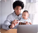 Uma pessoa com um bebê no colo, olhando para um teste de gravidez para ilustrar o tema pediatria