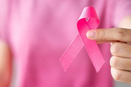 Pessoa com camisa rosa segura uma fita rosa, chamando atenção sobre a importância de discutir o câncer de mama no ambiente de trabalho no outubro rosa
