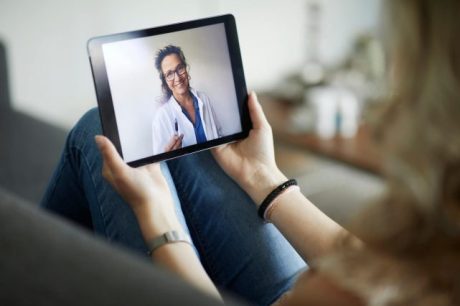 Pessoa sentada no sofá segura um tablet em videochamada médica, destacando a privacidade em consultas online seguras