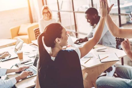 Em um ambiente de escritório, um grupo colabora em volta de uma mesa com laptops, papéis e outras pessoas. Ilustra a saúde emocional no ambiente de corporativo